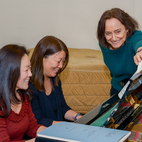 Two women taking a piano lesson with their teacher