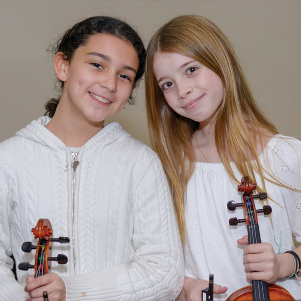 Two young girls holding violins and smiling