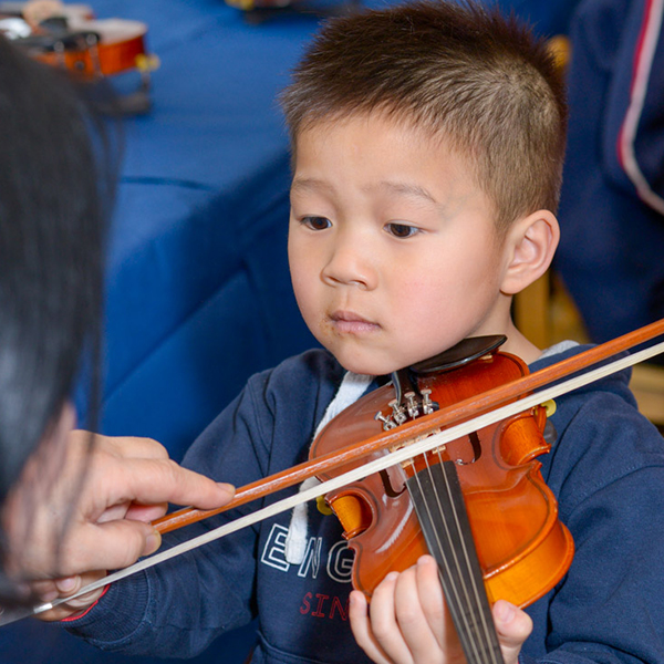 Young Asian toddler in a blue shirt playing the violin