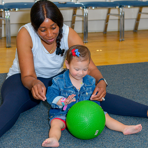 Young child rolling a green ball with her caretaker