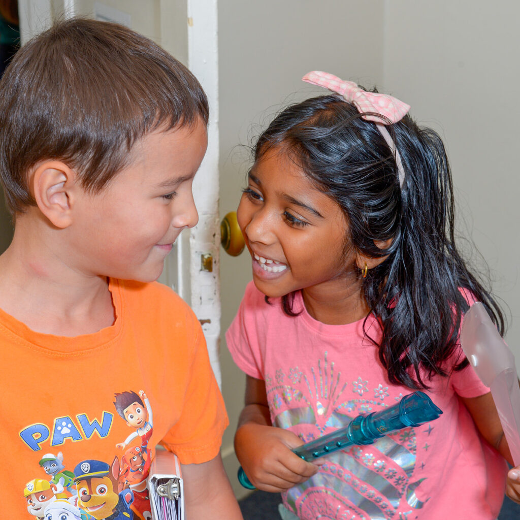 Young boy and girl smiling at one another holding recorders