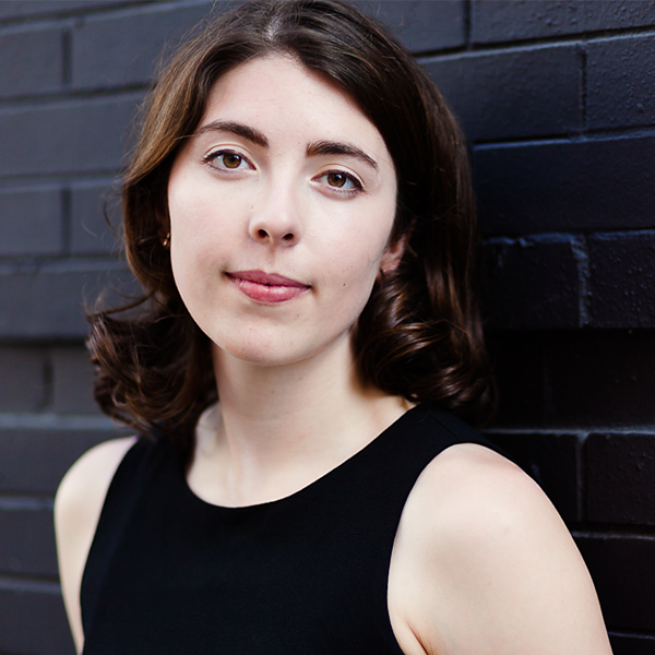 Compoer Flannery Cunningham wearing a black dress posed against a black brick wall