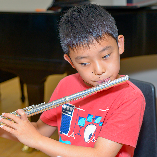 Young boy in red shirt playing the flute.