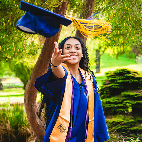 Girl smiling in graduation gown tossing her hat