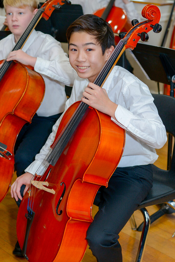 young boy holding a cello in an orchestra