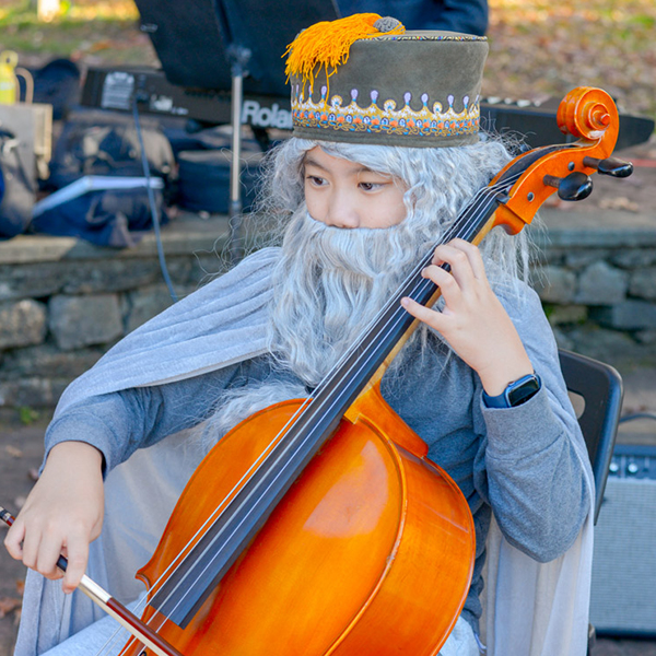 Young boy in a Halloween Costume playing the cello outdoors