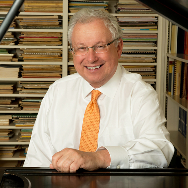 Man with grey hair, white shirt, yellow, tie seen through a piano with the lid open