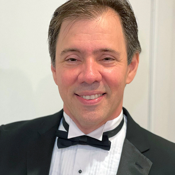Headshot of a man with dark hair smiling in a tuxedo