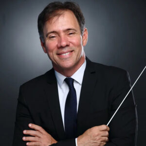 Leandro Gazineo in a suit and tie smiling and holding a conductor's baton