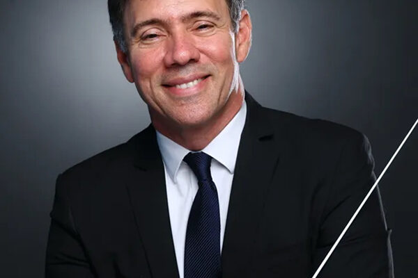 Leandro Gazineo in a suit and tie smiling and holding a conductor's baton