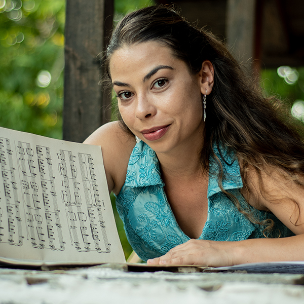 woman with long brown hair in a blue shirt looking at sheet music