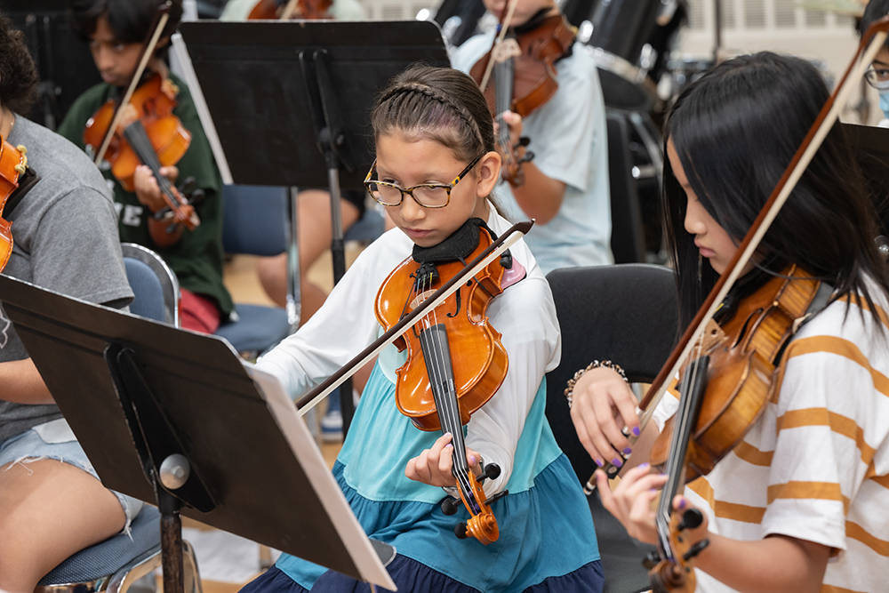 two young girls playing violin in an orchestra.
