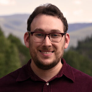 Man with brown hair, beard and mustache wearing glasses smiling