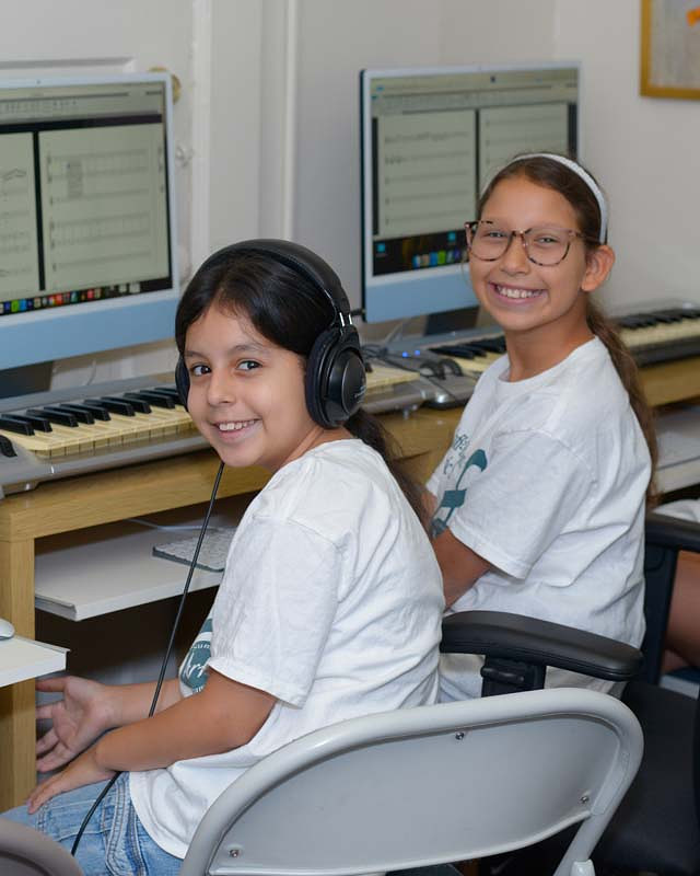 two girls sitting at computers with piano keyboards