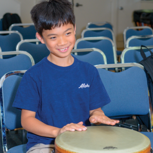 Young boy in blue shirt playing a drum