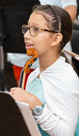 Young girl in a white sweater smiling and holding a violin