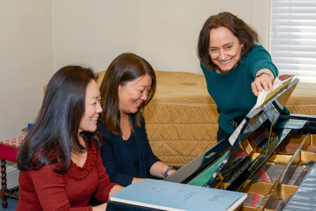 Three women smiling around a piano