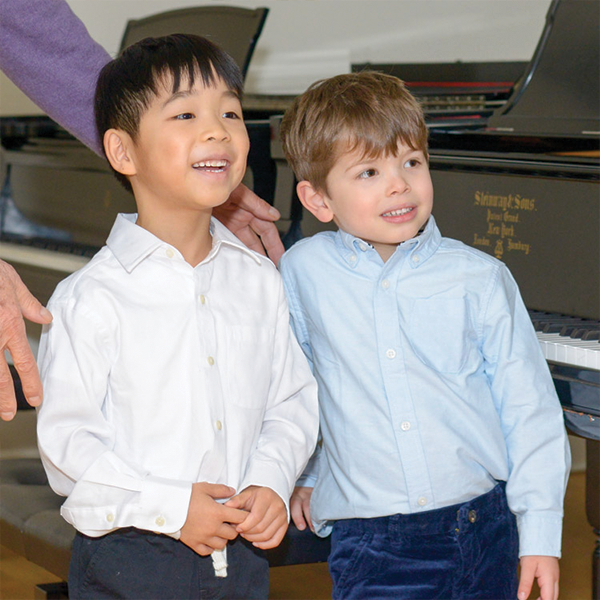 Two young boys smiling in front of a piano