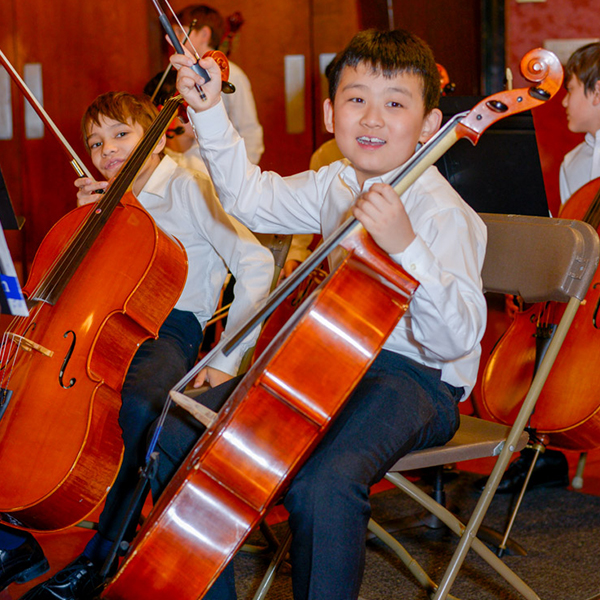 Young boys playing the cello in an orchestra