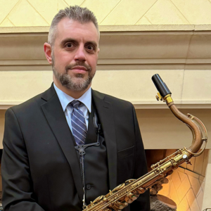 Tim Veeder dressed in a dark suit holding a saxophone