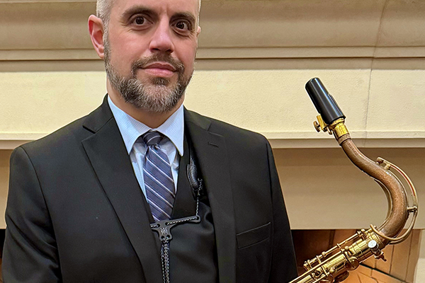 Tim Veeder dressed in a dark suit holding a saxophone