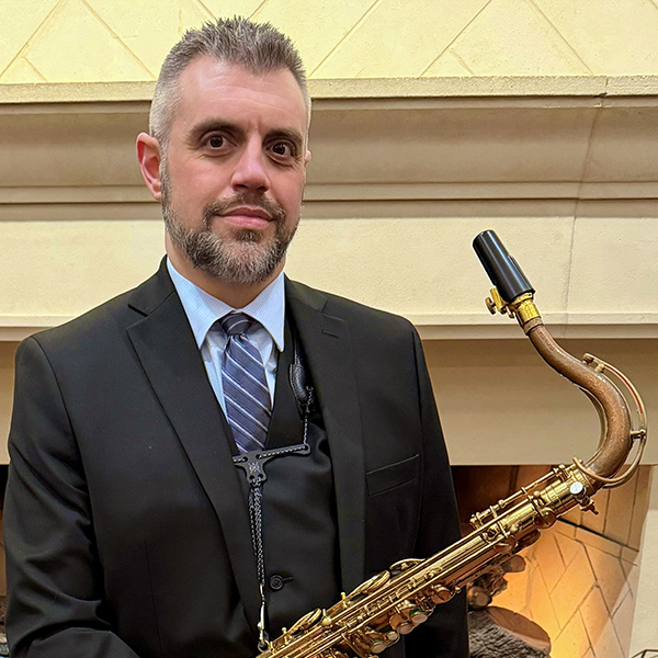 Tim Veeder dressed in a dark suit holding a saxophone