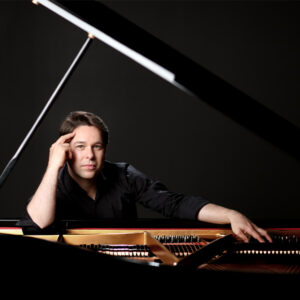 Pianist Victor Cayres dressed in black looking through an open piano