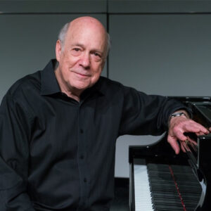 man in black shirt posing sideways at a piano