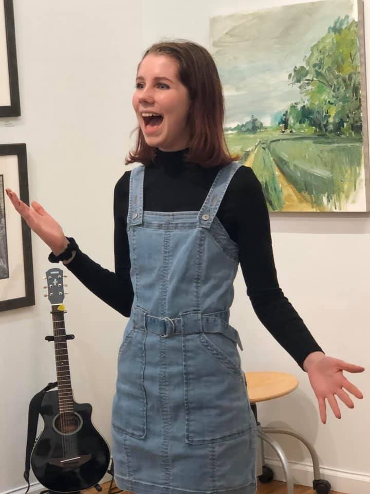 girl with shoulder length brown hair wearing a blue jumper singing