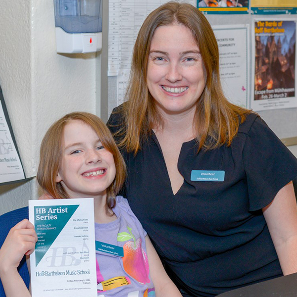 Blonde child holding a program and smiling with a blonde woman volunteer smiling