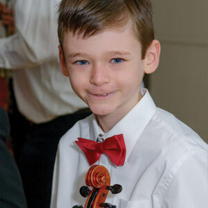 Young Boy with a red bow tie holding a violin and smiling